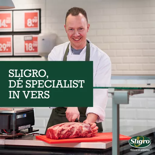 Visual for Sligro, featuring a smiling specialist preparing a large cut of fresh meat in a professional kitchen setting, with the text 'Sligro, dé specialist in vers' (Sligro, the specialist in fresh).