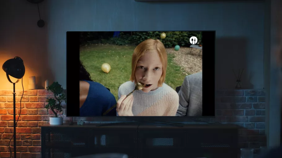 Photo of a tv screen in a dark living room playing Foodbag's promotional video featuring a red haired girl with a fork in her mouth.
